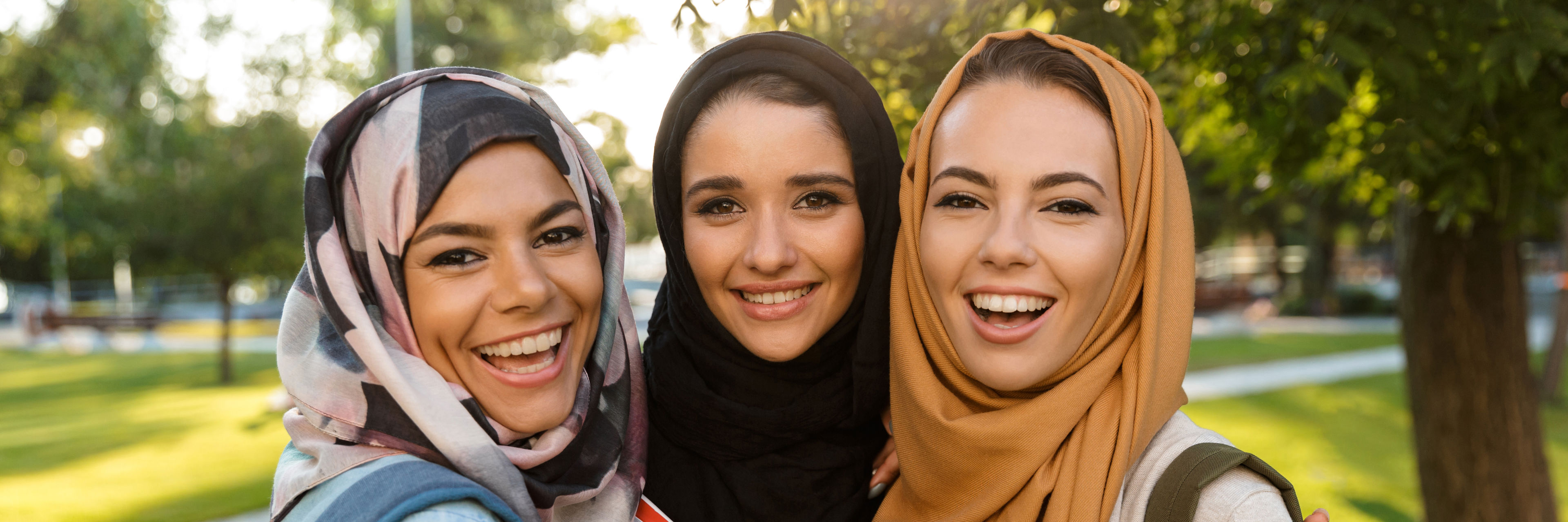 Tre kvinder iført hijab udenfor i sollys